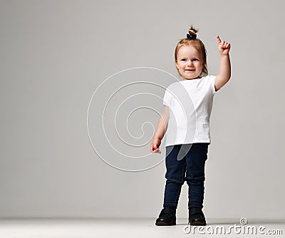 Toddler child baby girl kid standing in white free text space t-shirt pointing finger up Stock Photo