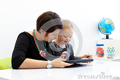 Toddler girl in child occupational therapy session doing playful exercises on a digital tablet with her therapist. Stock Photo