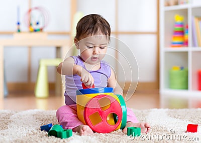 Toddler girl playing indoors with sorter toy sitting on soft carpet Stock Photo