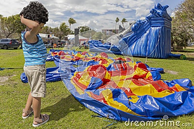 A toddler scratches his head while he stands next to a deflated bounce house Stock Photo