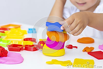 Toddler sculpts from colored plasticine on a white table. Stock Photo