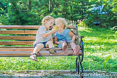 Toddlers boy and girl sitting on a bench by the sea and eat an a Stock Photo