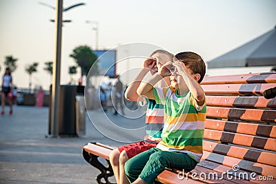 Toddlers boy and his sibling brother sitting on a bench by the c Stock Photo