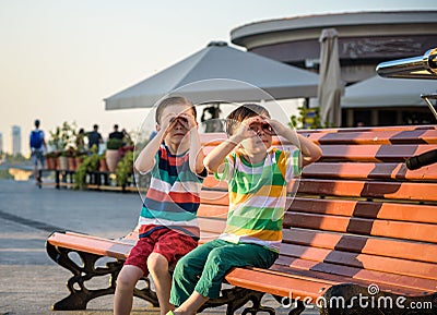 Toddlers boy and his sibling brother sitting on a bench by the city Stock Photo