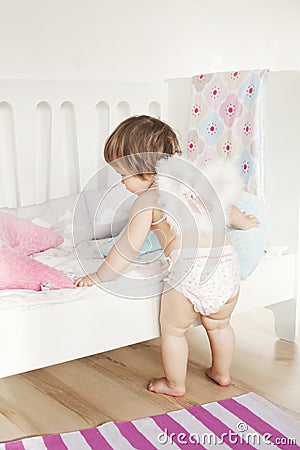 Todler baby girl in nappy and angel wings plays near bed. Interior design of children`s room in light colors Stock Photo