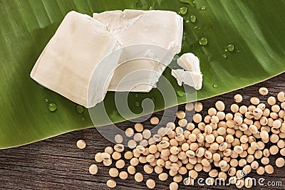 Tofu on green leaf with drops and soybeans on wood background. Stock Photo