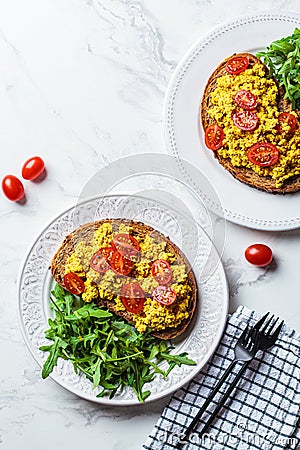 Tofu scramble toast with tomatoes and arugula on white plate, white marble background. Vegan food concept Stock Photo