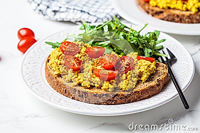 Tofu scramble toast with tomatoes and arugula on white plate, white marble background. Vegan food concept Stock Photo