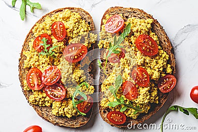 Tofu scrambled toast with tomatoes and arugula, white marble background. Plant based diet concept Stock Photo