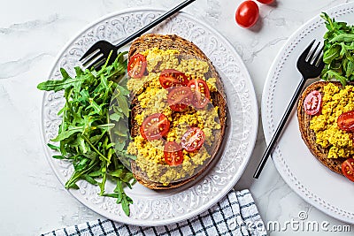 Tofu scrambled toast with tomatoes and arugula on white plate, white marble background. Vegan food concept Stock Photo