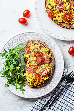 Tofu scrambled toast with tomatoes and arugula on white plate, white marble background. Vegan food concept Stock Photo