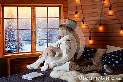 Mother and children rest in a country house. Together they lie on the bed and shoot out the window to the snow forest. Stock Photo