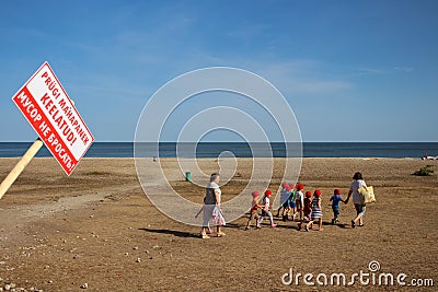 Two women lead small children in red bandanas to the sea. The inscription on the sign Editorial Stock Photo