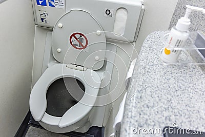 The toilet seat with the lid open at a aircraft lavatory. With a tissue dispenser and flush button above Stock Photo