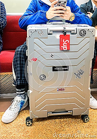 Tokyo, Japan 10.02.2018 bright stylish aluminum suitcase with stickers next to fashionably dressed young man sitting in subway Editorial Stock Photo