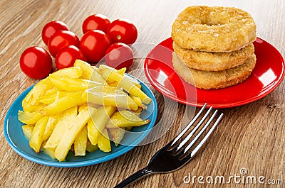 Tomatoes, fried potato in plate, stack of chicken donut in plate, fork on wooden table Stock Photo