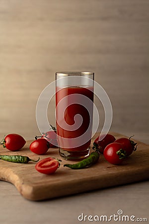 Tomato juice in a tall glass glass, cherry tomatoes, hot peppers on a cutting board, wooden background. Studio shot Stock Photo