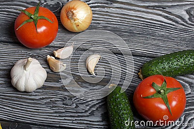 Tomatoes with green ponytails, onion and garlic head. Two green prickly cucumbers with yellow flowers. They lie on the surface of Stock Photo