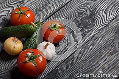 Tomatoes with green ponytails, onion and garlic head. Two green prickly cucumbers with yellow flowers. They lie on the surface of Stock Photo