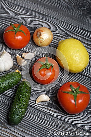 Tomatoes with green ponytails, onion, lemon and garlic head. Two green prickly cucumbers with yellow flowers. They lie on the Stock Photo