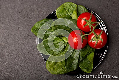 Tomatoes and spinach leaves on black plate, top view Stock Photo