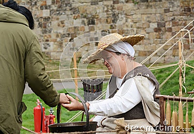 Woman dressed in Medieval clothes guides a visitor in candlemaking Editorial Stock Photo