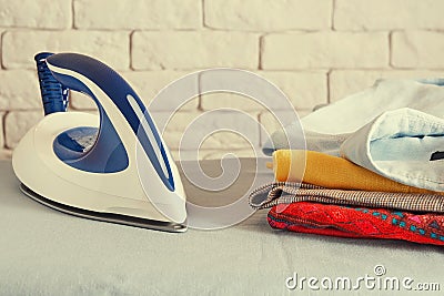 Toned image of house appliances with iron and stack of clothes on ironing board Stock Photo