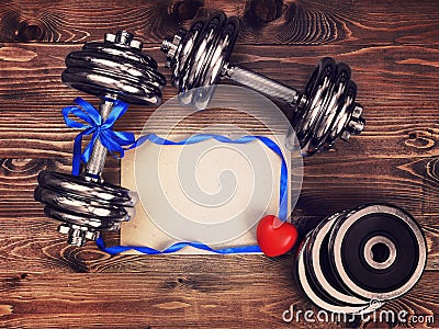 Toned image of metal dumbbells, blue atlas ribbon, red heart and a sheet of craft paper Stock Photo