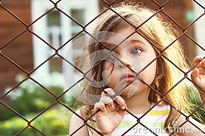 Toned portrait of Sad cute little girl looks through wire fence Stock Photo