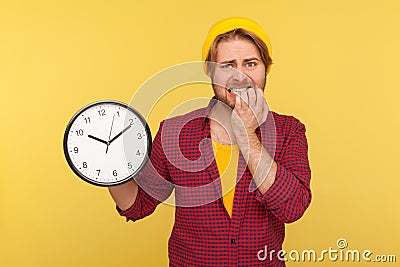 Too late! Portrait of impatient anxious hipster guy in checkered shirt holding big clock and biting nails, nervous Stock Photo