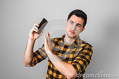 Too much talk. young man in yellow shirt annoyed by a voice on phone, gesturing with one hand against on grey background Stock Photo