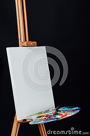 Tools of the artist. Brushes, wooden easel tripod, palette colorful. Black background, studio, nobody. Stock Photo