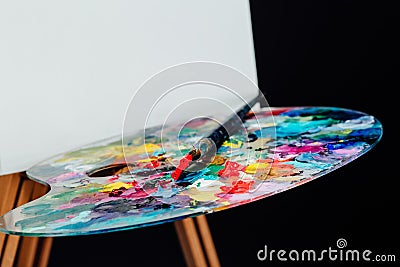 Tools of the artist. Brushes, wooden easel tripod, palette colorful. Black background, studio, nobody. Stock Photo