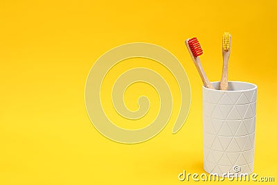Toothbrushes made of bamboo in holder on yellow background. Space for text Stock Photo