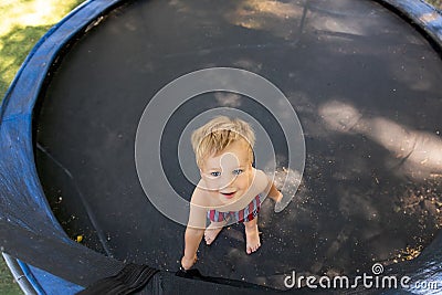 Top above view of cute little caucasian funny blond toddler boy stand inside big black trampoline at home backyard Stock Photo