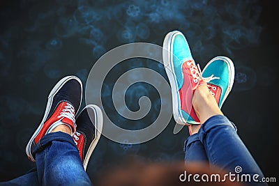 Top close up view of young couple legs in sneakers sitting on pier near to the sea full of jellyfish Stock Photo