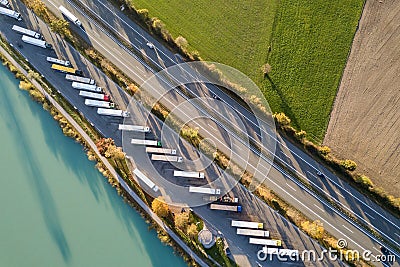 Top down aerial view of highway interstate road with fast moving traffic and parking lot with parked lorry trucks Stock Photo