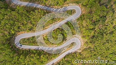 TOP DOWN: Scenic shot of a car driving along empty road winding through a forest Stock Photo