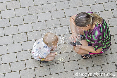 Top-down view on child drawing on paving slabs and woman watching him. Stock Photo