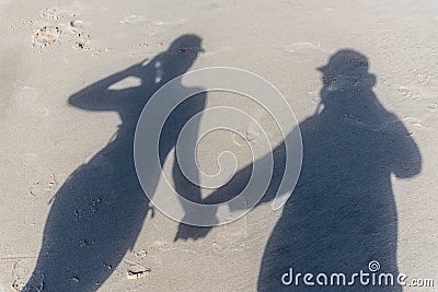 The top down view of a familys shadows on the beach sand. A man in a hat is holding hands with a woman in a bikini and cap Stock Photo