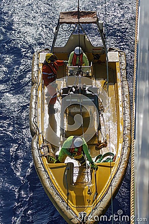 Top down view of launching or recovering yellow Fast Rescue Boat (FRC) from ship. Three crew members onboard. Stock Photo