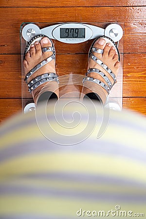 Top down view of an obese women wearing sandals standing on top of a weighing scale Stock Photo