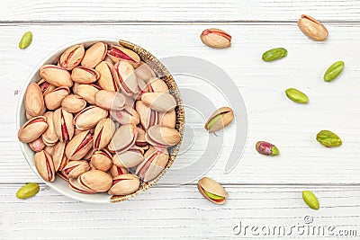 Top down view, porcelain bowl with turkish red pistachio nuts, some green seeds scattered on white boards desk around Stock Photo