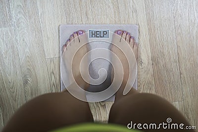 Top-down view to female bare feet standing on scale with written word Help on display. Concept of fitness and loosing weight. Stock Photo