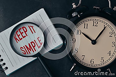 Top view of alarm clock, magnifying glass and notebook written with text KEEP IT SIMPLE Stock Photo
