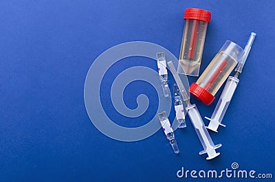 Top view of ampules, syringes and plastic urine containers with samples on the dark blue background.Empty space for text.Concept o Stock Photo