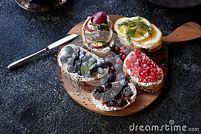 Top view of appetizing bruschetta with cream cheeses. Garnished with blueberries, lemon, ripe pomegranate and apple Stock Photo