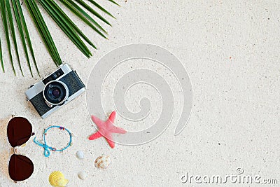 Top view of beach sand with coconut leaves, camera, bracelet made of seashells, sunglasses, shells and starfish. Stock Photo