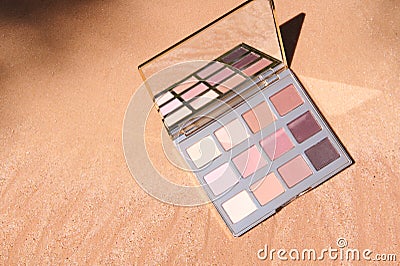 Top view. Makeup palette of eyeshadows with gradient from dark brown to shades of beige color on golden sandy background Stock Photo