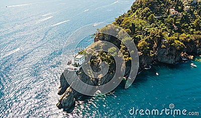 Top view of a beautiful sea coast with a white lighthouse, green trees and palm trees on top of a cliff surrounded by sea water Stock Photo